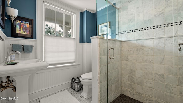 full bathroom featuring toilet, a shower stall, ornamental molding, and wainscoting