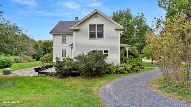 rear view of property with a shingled roof, a lawn, and a chimney