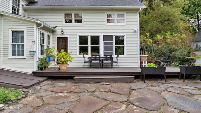 back of property with roof with shingles, outdoor dining area, a patio, and a wooden deck