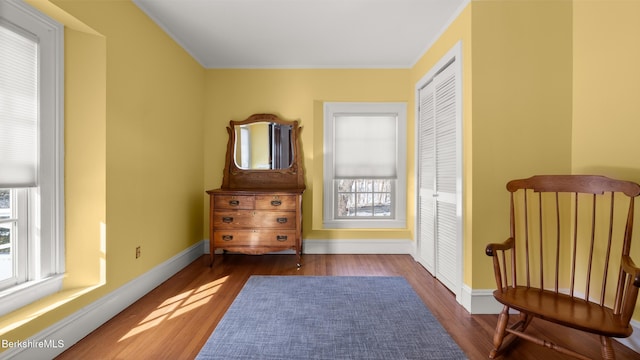 living area with a healthy amount of sunlight, baseboards, wood finished floors, and ornamental molding