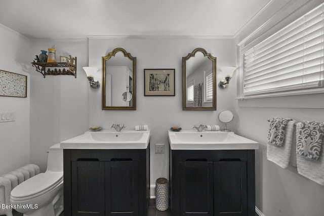 bathroom featuring two vanities, toilet, ornamental molding, and a sink
