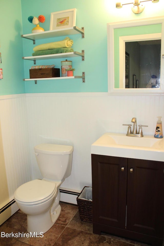 bathroom featuring wooden walls, toilet, vanity, and a baseboard heating unit