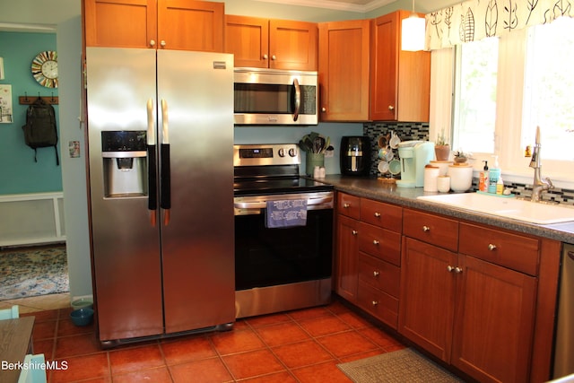 kitchen with tile patterned floors, sink, ornamental molding, decorative light fixtures, and stainless steel appliances