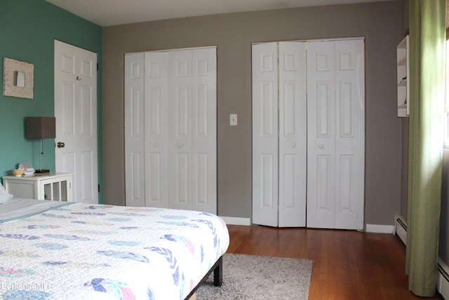 bedroom featuring baseboard heating, multiple closets, and dark hardwood / wood-style floors