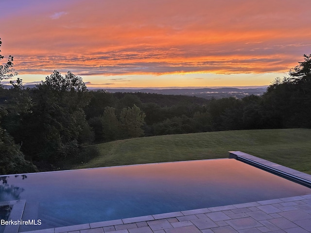 pool at dusk with a yard and a forest view