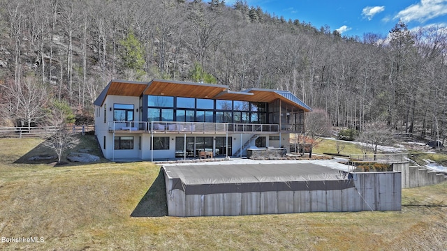 back of house with stairway, fence, a view of trees, a deck, and a lawn