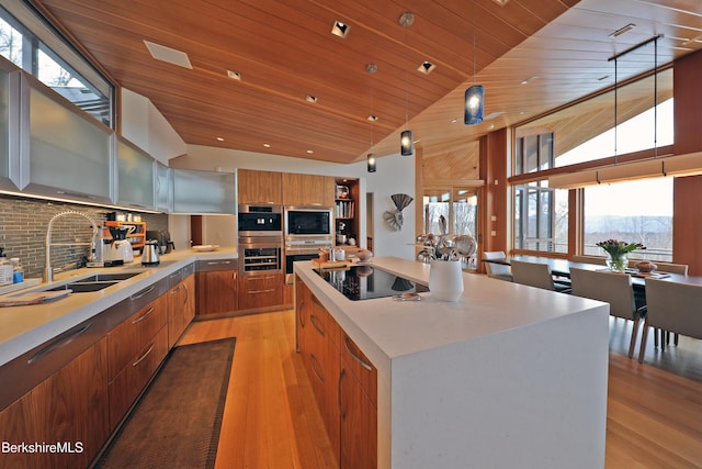 kitchen with brown cabinets, modern cabinets, a sink, a center island, and black electric cooktop