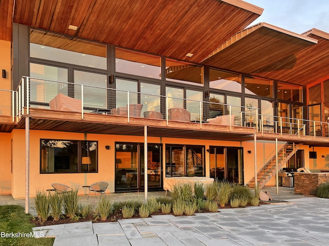 rear view of property featuring stucco siding, a balcony, stairway, and a patio area