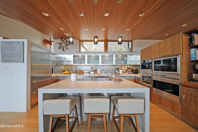 kitchen with tasteful backsplash, glass insert cabinets, light countertops, stovetop, and brown cabinets