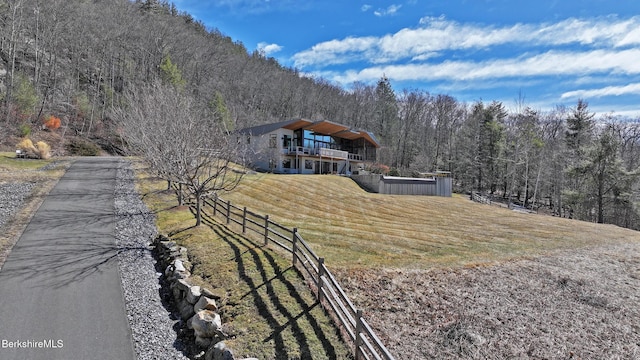 view of front of house featuring a balcony, a wooded view, a front yard, and fence