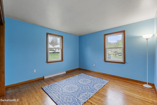 spare room featuring baseboard heating, plenty of natural light, wood finished floors, and baseboards
