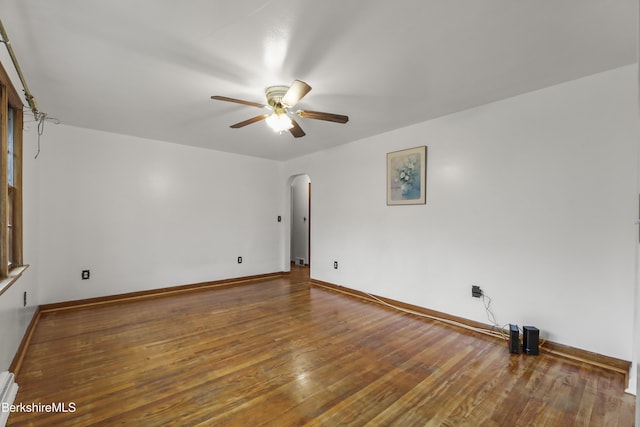 empty room with ceiling fan, arched walkways, baseboard heating, and baseboards
