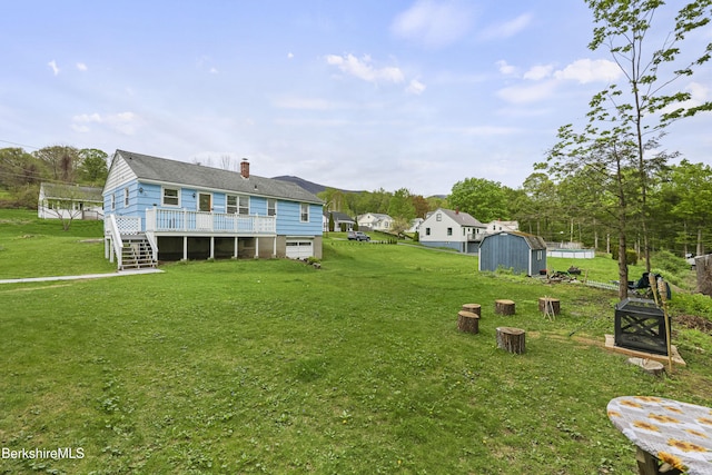 back of house featuring a storage shed, a wooden deck, a yard, and an outdoor structure