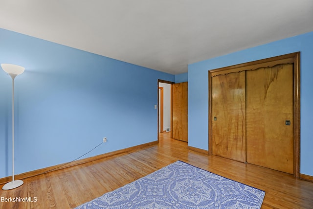 unfurnished bedroom featuring wood finished floors, baseboards, and a closet