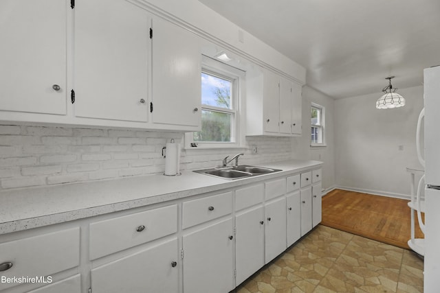 kitchen with a sink, decorative backsplash, white cabinets, light countertops, and freestanding refrigerator