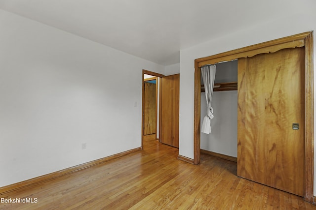 unfurnished bedroom with light wood-type flooring, baseboards, and a closet