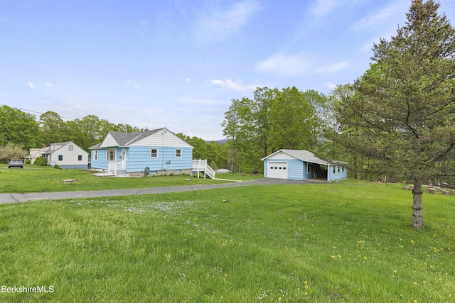 view of grassy yard featuring a detached garage, an outdoor structure, and driveway