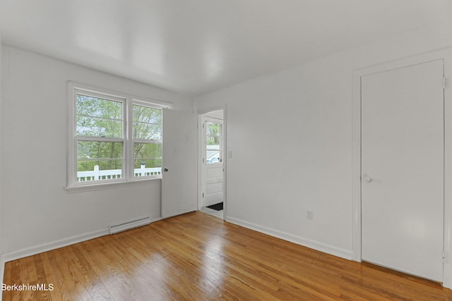 unfurnished room with a baseboard heating unit, wood finished floors, and baseboards