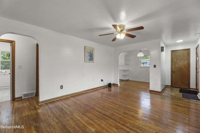 unfurnished living room with arched walkways, a ceiling fan, hardwood / wood-style floors, and baseboards