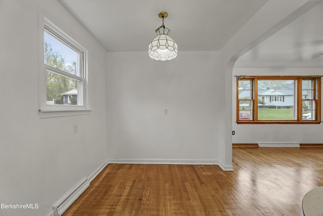 unfurnished dining area with baseboard heating, arched walkways, wood finished floors, and baseboards