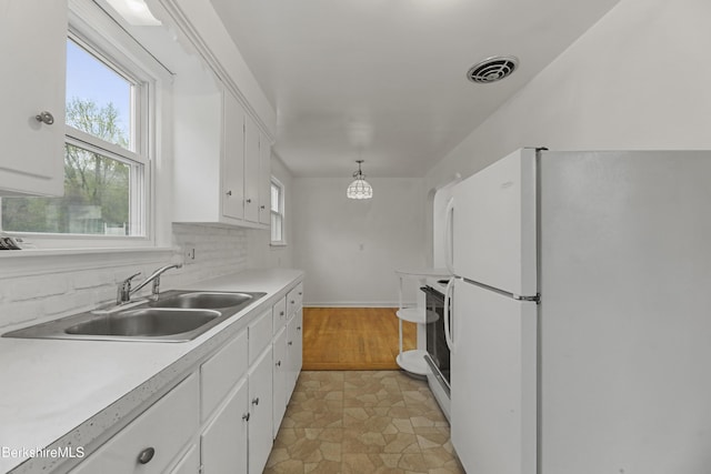 kitchen with freestanding refrigerator, a sink, white cabinetry, light countertops, and tasteful backsplash