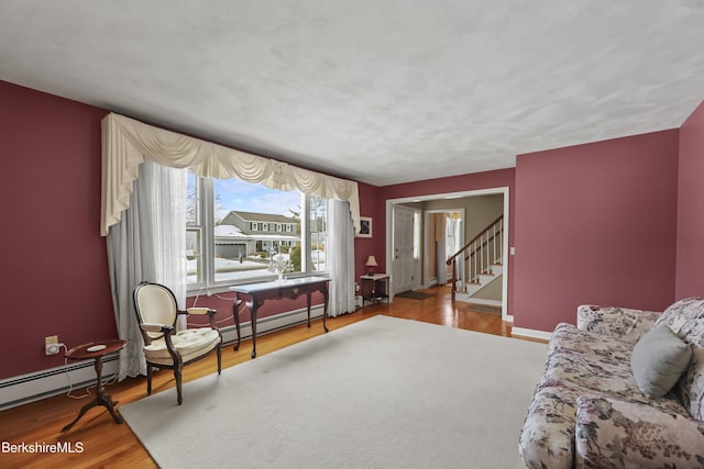 living area with stairs, a baseboard radiator, wood finished floors, and baseboards