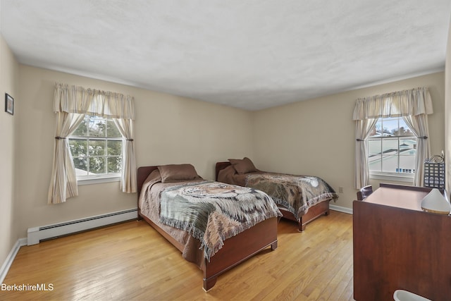 bedroom with baseboard heating, light wood-type flooring, and baseboards