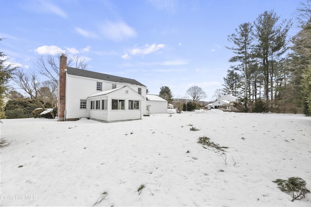 snow covered house with a sunroom and a chimney