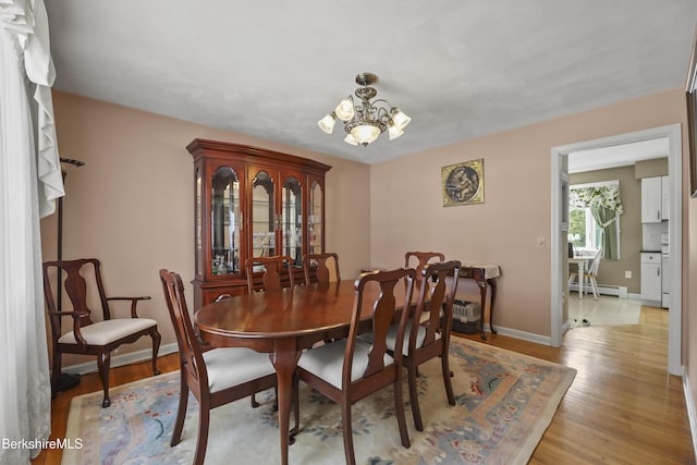 dining space with a chandelier, baseboard heating, baseboards, and light wood-style floors