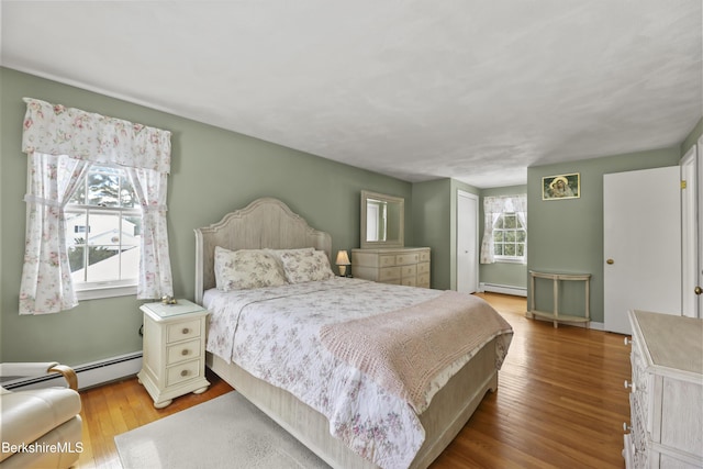 bedroom with a baseboard heating unit, multiple windows, baseboard heating, and wood finished floors