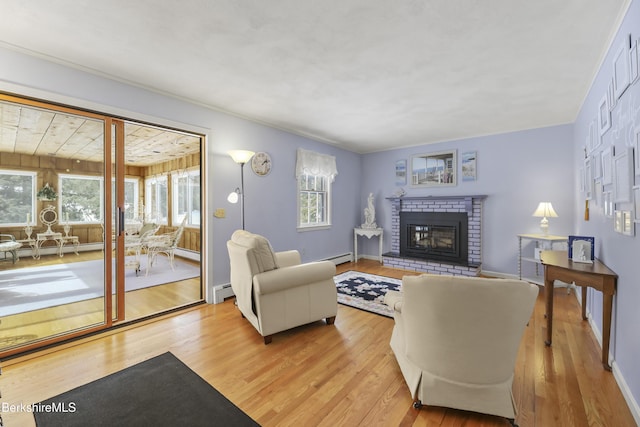 living area featuring a baseboard heating unit, a fireplace, baseboards, baseboard heating, and light wood finished floors