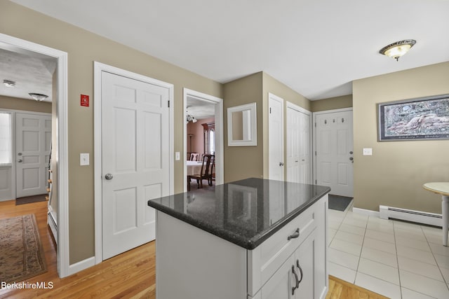 kitchen with baseboards, dark stone counters, a baseboard radiator, a kitchen island, and white cabinetry