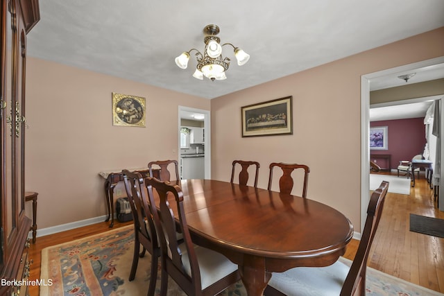 dining space with baseboards, wood finished floors, and an inviting chandelier