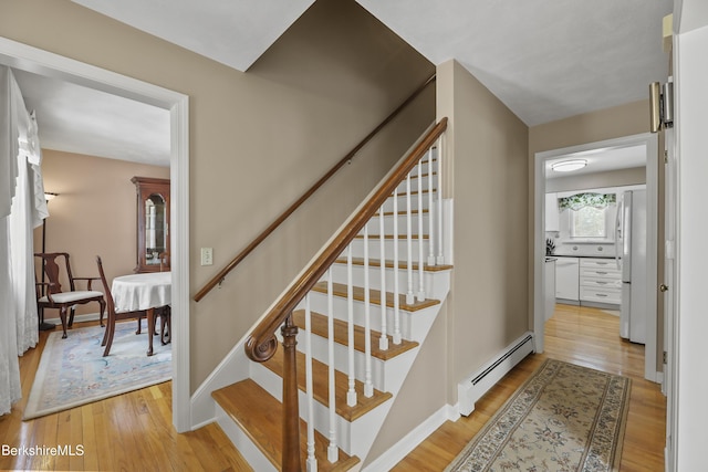 staircase with baseboards, baseboard heating, and wood finished floors