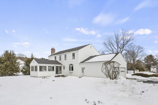 snow covered back of property with a garage, a chimney, and a sunroom