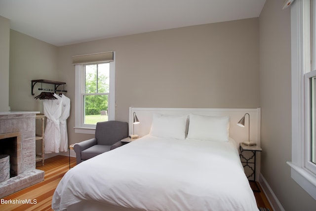 bedroom with a brick fireplace, baseboards, and wood finished floors