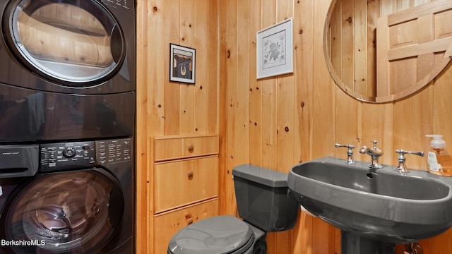 laundry room with wooden walls, laundry area, stacked washer / drying machine, and a sink