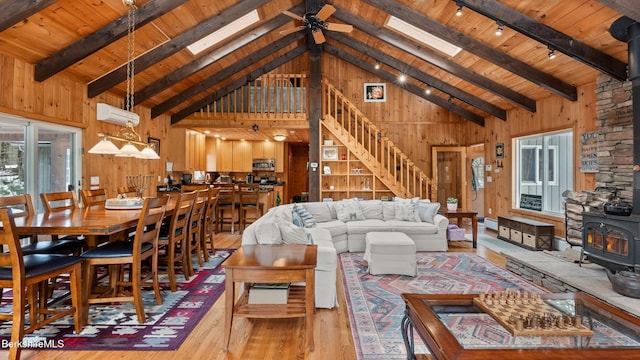 living room featuring a wood stove, wooden walls, a ceiling fan, and beamed ceiling