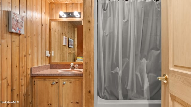 full bath with wooden walls, vanity, and shower / bath combo