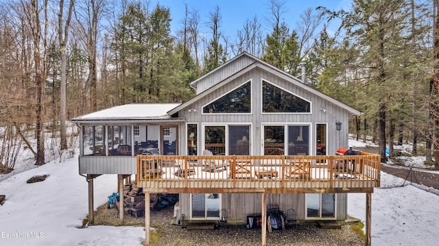 snow covered back of property with a deck and a sunroom