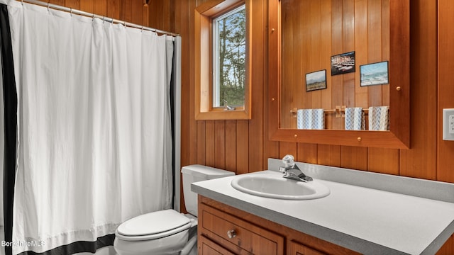 bathroom featuring toilet, a healthy amount of sunlight, wood walls, and vanity