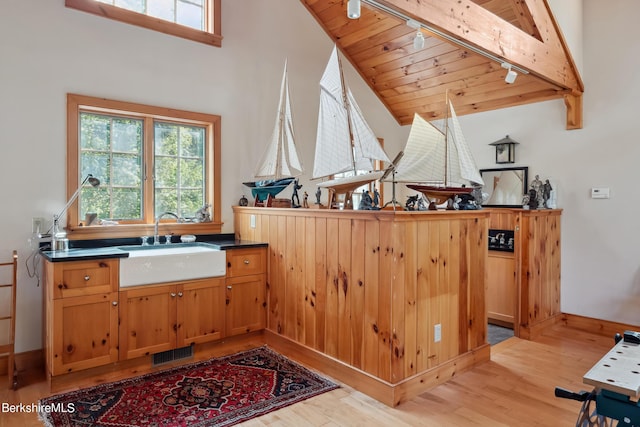 interior space with kitchen peninsula, wood ceiling, sink, lofted ceiling with beams, and light hardwood / wood-style floors