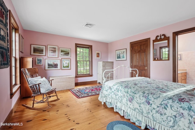 bedroom featuring ensuite bath, light hardwood / wood-style floors, and multiple windows