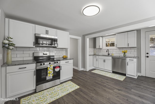 kitchen featuring dark wood-style flooring, a sink, appliances with stainless steel finishes, dark countertops, and backsplash