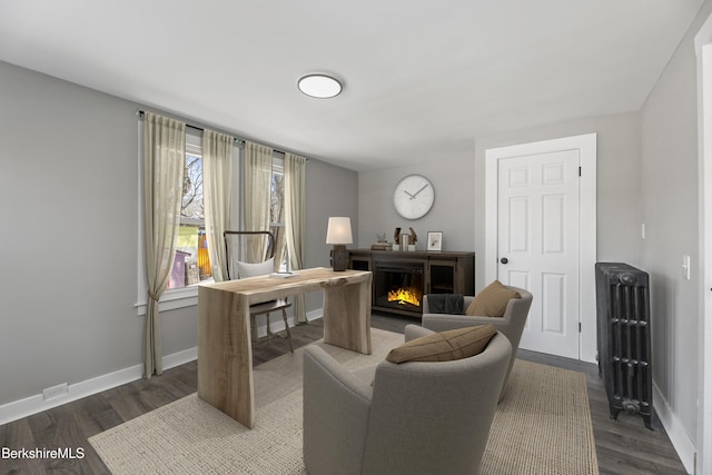 office featuring a glass covered fireplace, dark wood-style floors, and baseboards