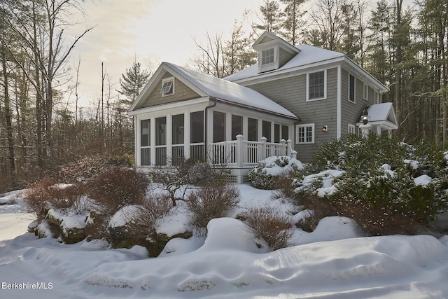 snow covered rear of property with a sunroom