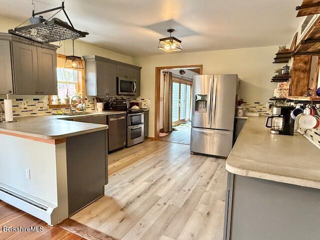 kitchen with a peninsula, light countertops, a sink, light wood-style flooring, and appliances with stainless steel finishes