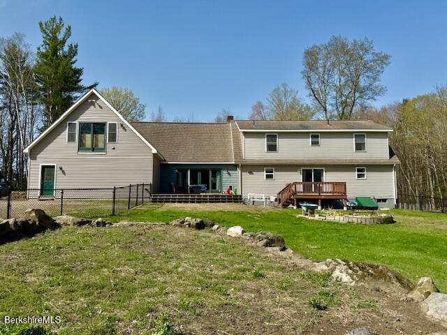 back of property with fence, a wooden deck, and a yard