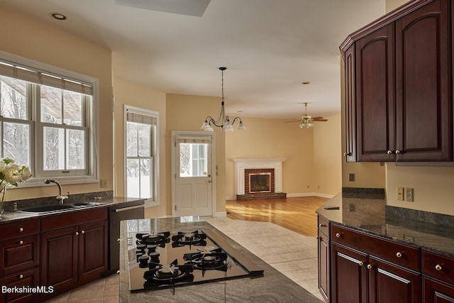 kitchen featuring sink, a brick fireplace, pendant lighting, dark stone counters, and black gas stovetop