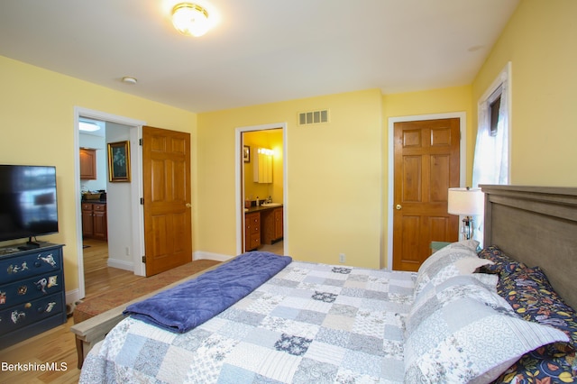 bedroom featuring light wood-style floors, baseboards, visible vents, and connected bathroom